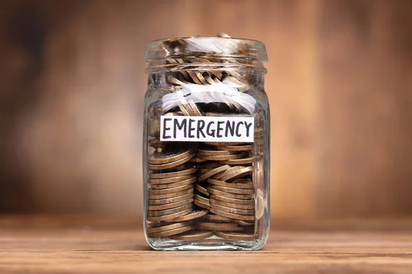 Jar labeled 'Emergency Fund' with coins and a financial checklist on a desk.